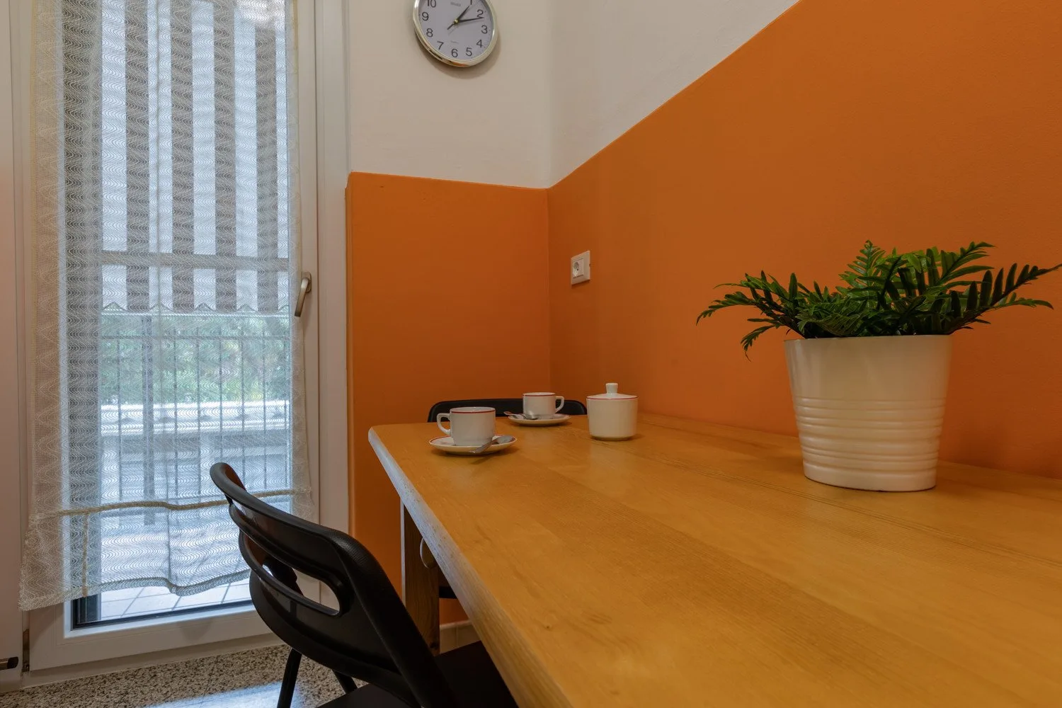 Un comedor luminoso con una mesa de madera, tazas y una planta en maceta.