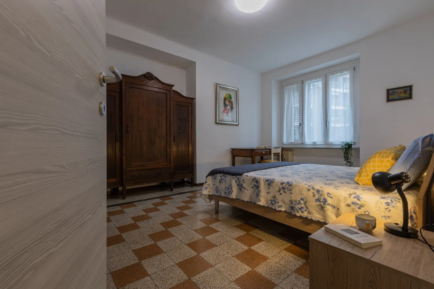 Un dormitorio con una cama doble, un armario y una ventana con cortinas translúcidas.