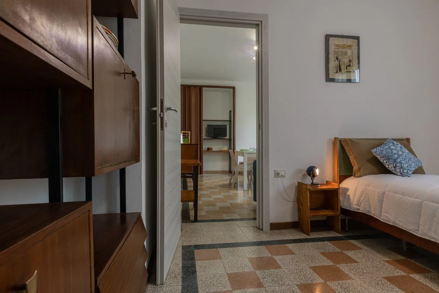 Un dormitorio con una cama, una mesita de noche y una puerta abierta a otra habitación.