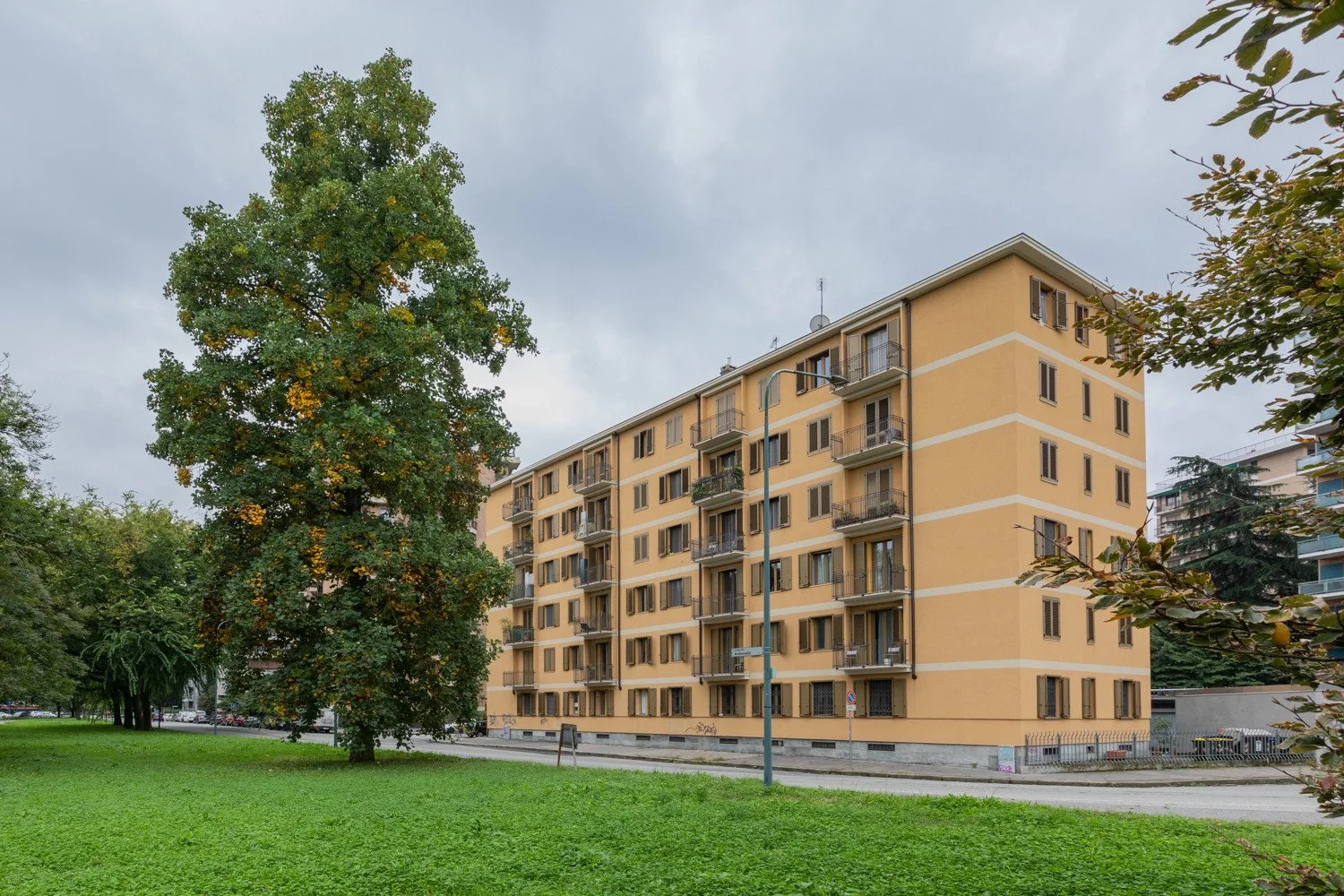 Un edificio de apartamentos de varios pisos se alza junto a un césped verde y árboles maduros.