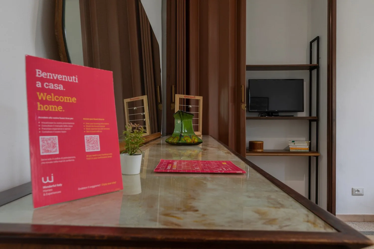 Una habitación estrecha con una encimera de mármol, un jarrón de vidrio verde y un televisor en una estantería.