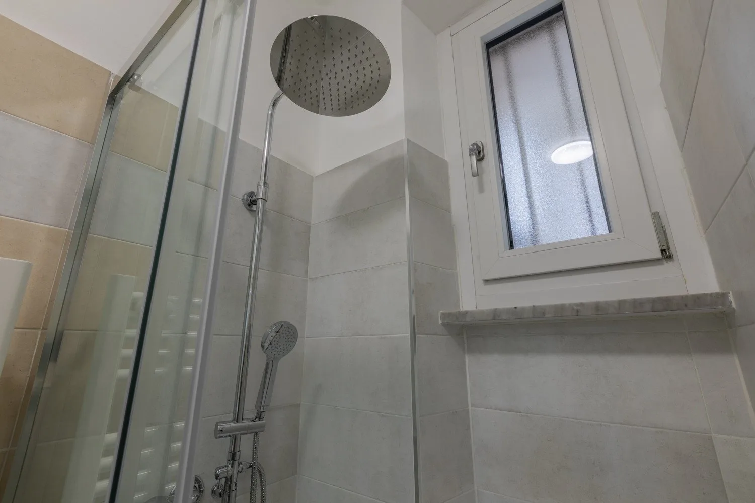 Zona de ducha de baño con azulejos y una ventana esmerilada.