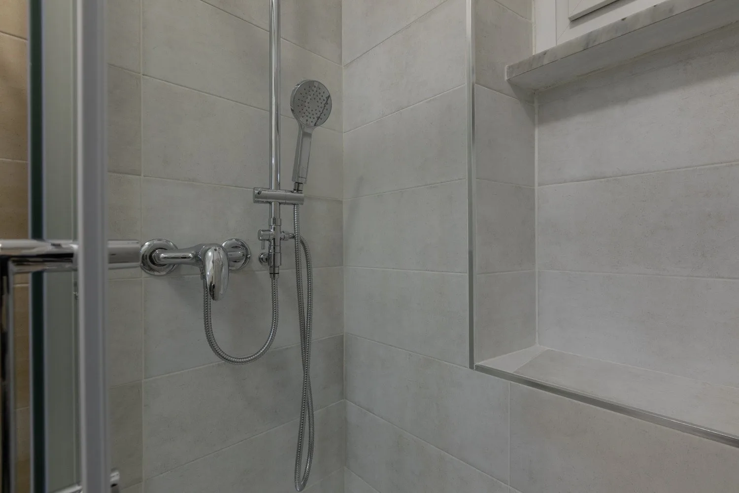 Una ducha de baño alicatada con cabezal de mano y estante empotrado.