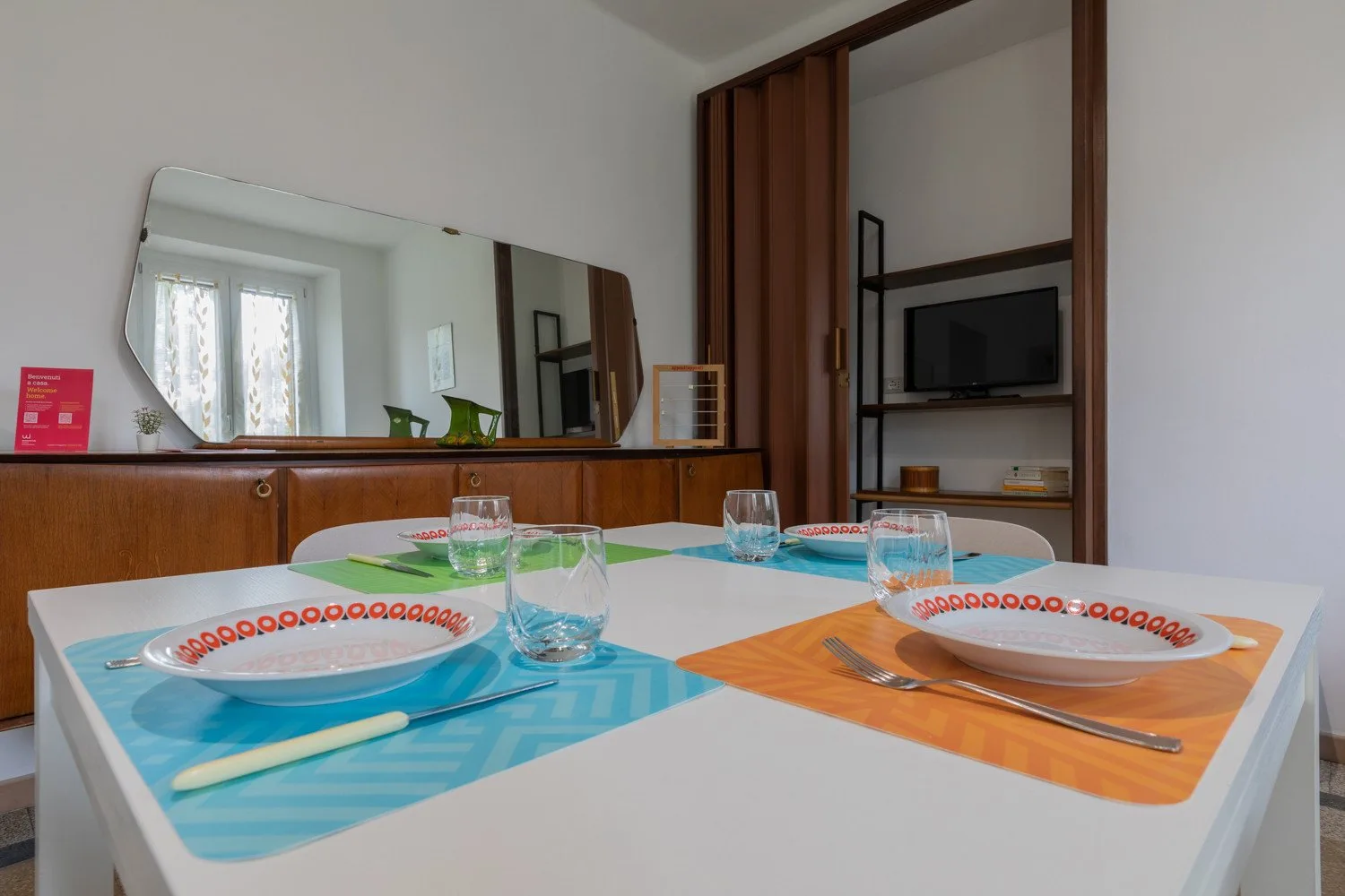 Una mesa de comedor está puesta con platos, vasos y manteles individuales coloridos.