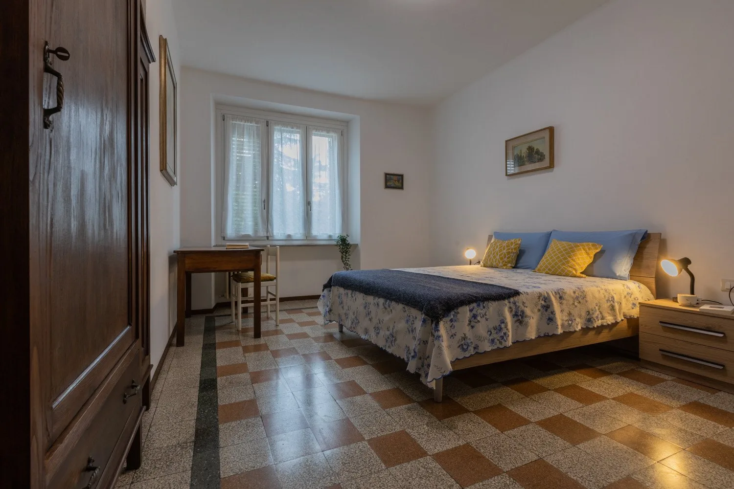 Un dormitorio con una cama doble, mesillas de noche y un escritorio bajo la ventana.