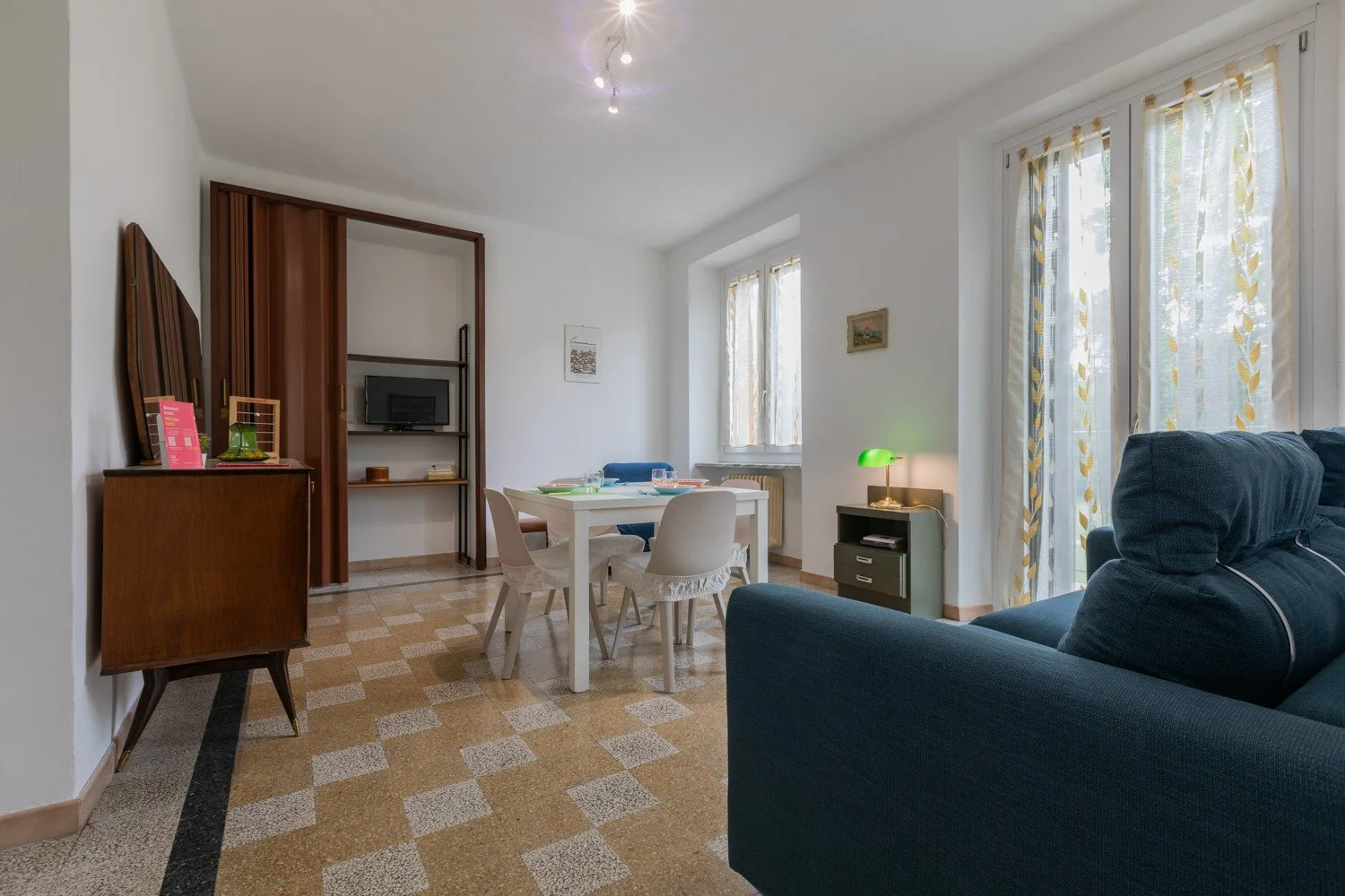 Una luminosa sala de estar y comedor tiene una mesa, asientos y grandes ventanas.