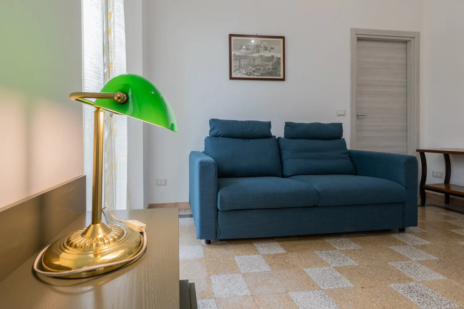 Una sala de estar con asientos azules, una lámpara de latón y un cuadro enmarcado.