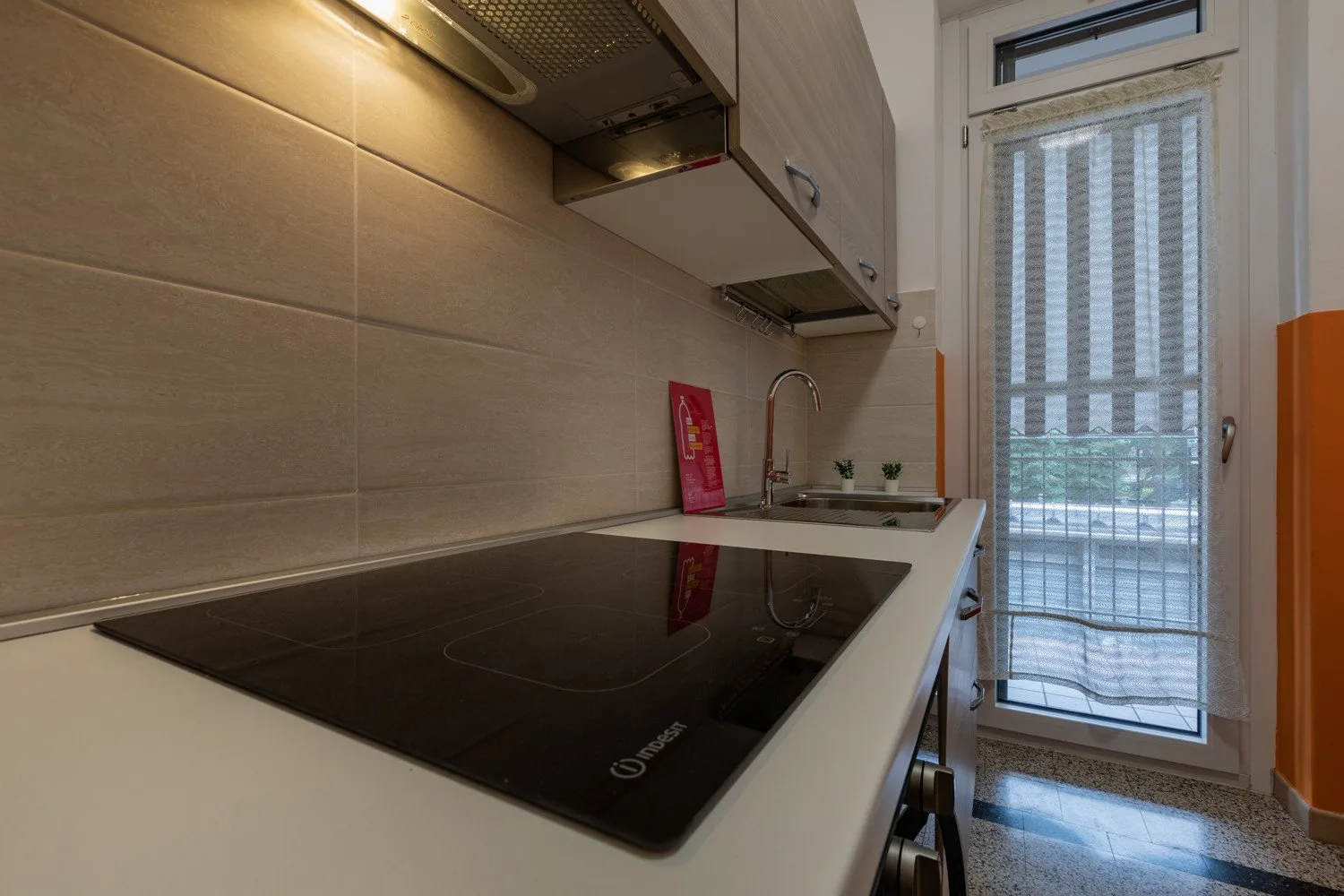Una cocina moderna con una placa negra, fregadero y ventana alta.