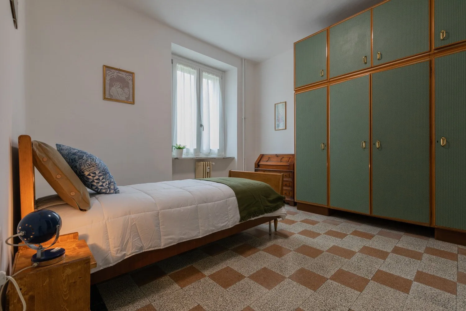 Un dormitorio con una cama junto a armarios verdes y una ventana.