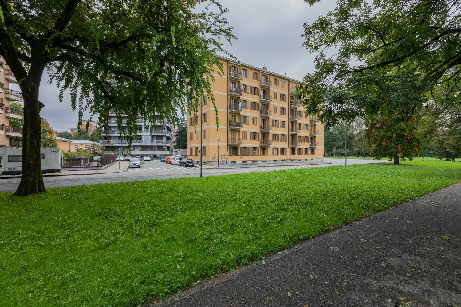 Un edificio residencial está junto a un parque con césped y un sendero pavimentado.