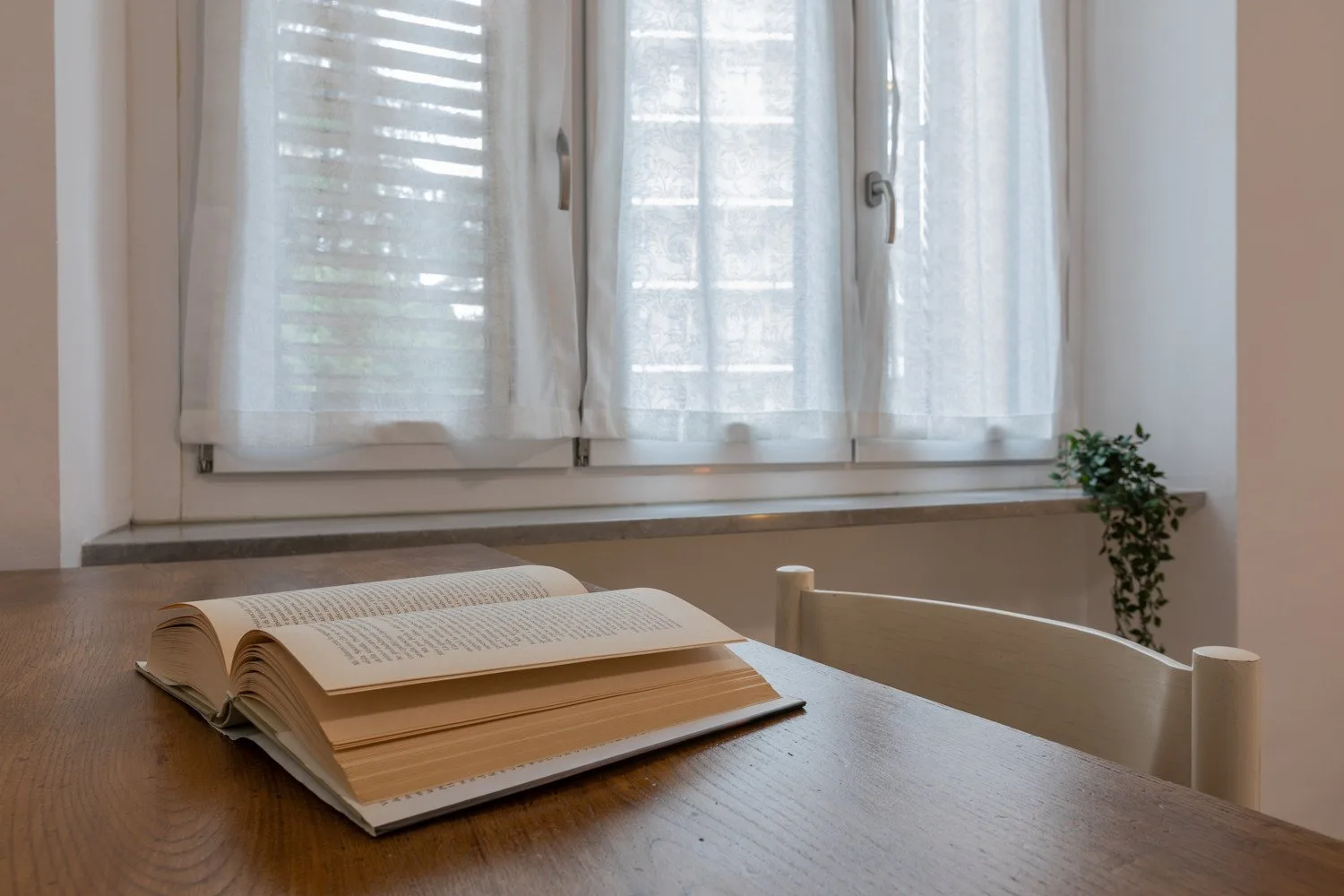 Una mesa junto a una ventana luminosa, con un libro abierto encima.