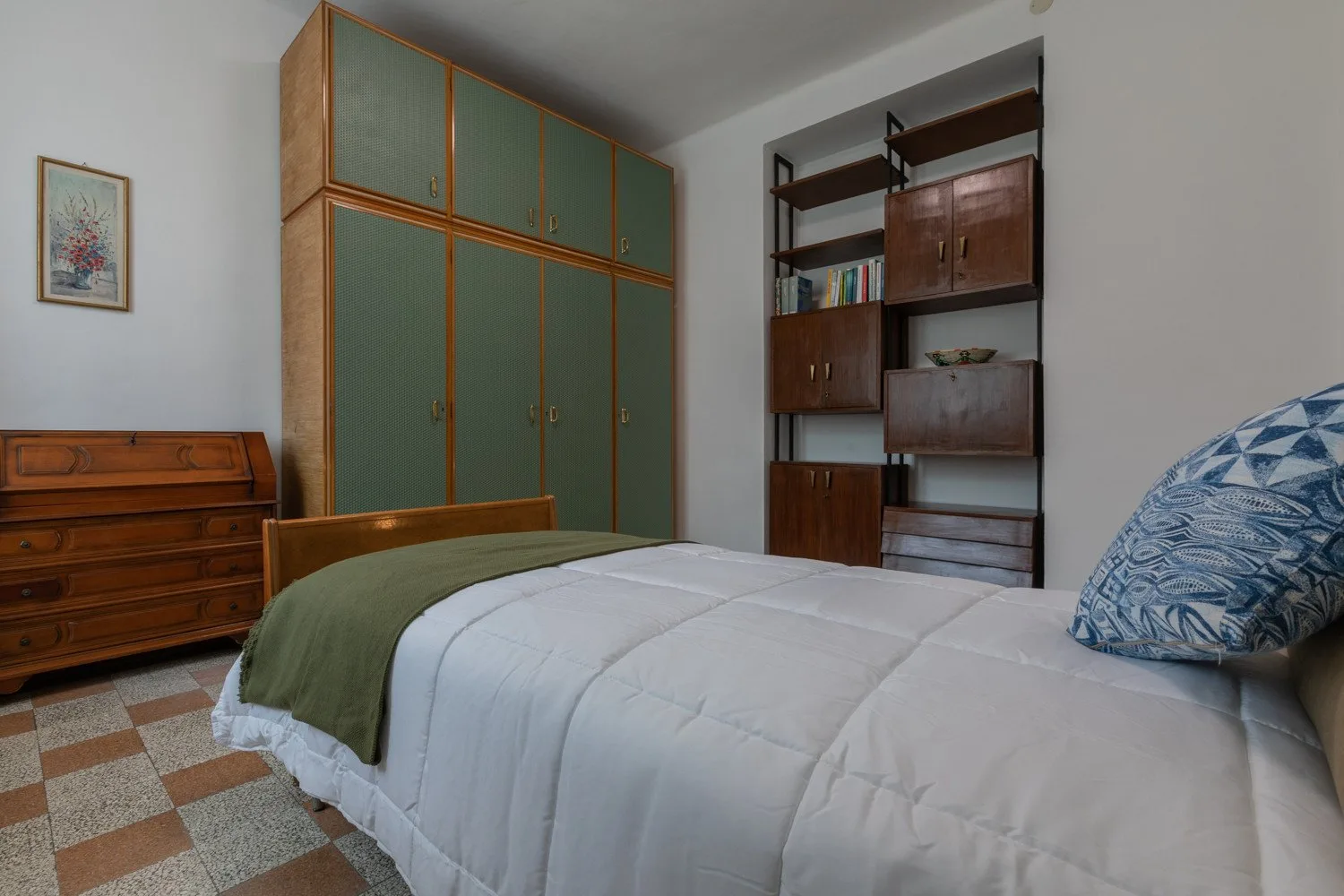 Un dormitorio con una cama, armarios verdes y estanterías de madera.