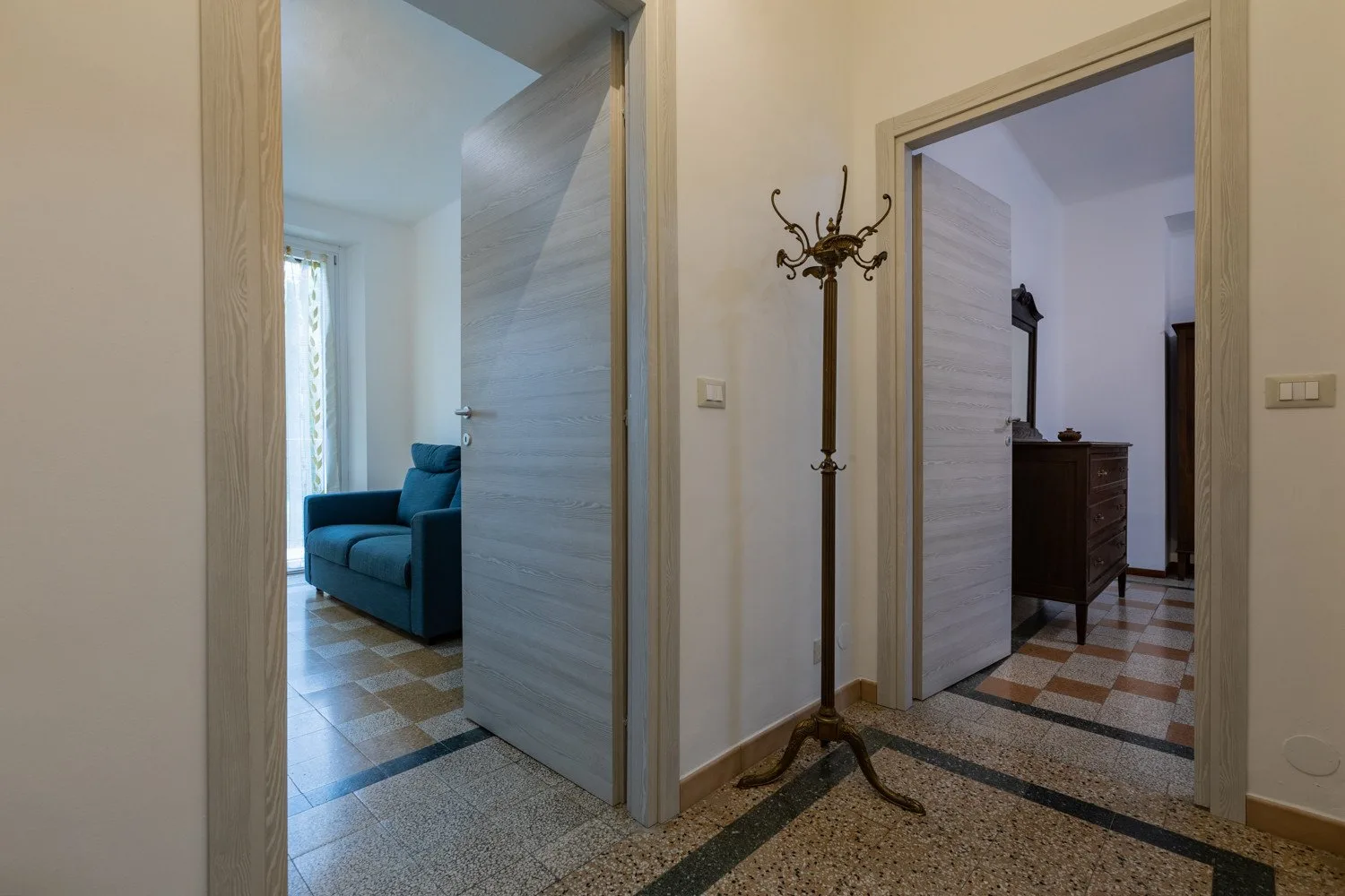 Un pasillo con puertas abiertas deja ver una zona con asientos azules y una habitación con una cómoda.