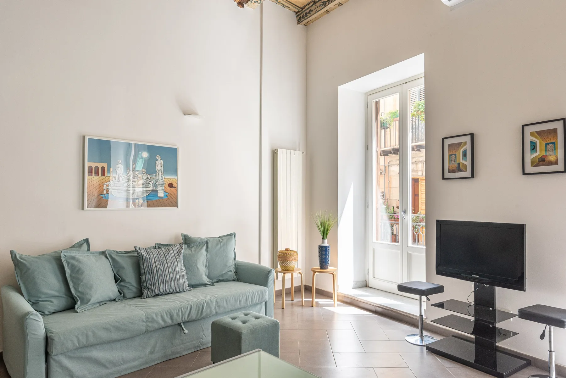 Una sala luminosa con un sofá verde, un televisor y ventanas altas.