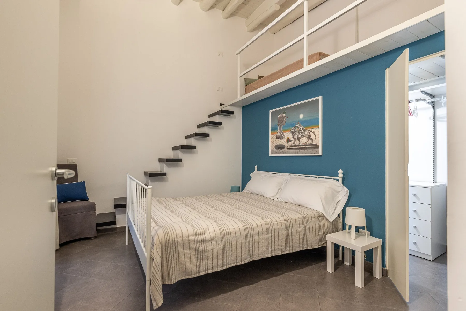 Un dormitorio con una cama doble bajo una pared azul y una plataforma elevada.