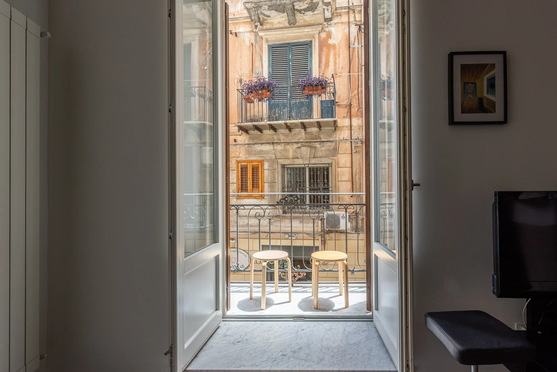 Una puerta abierta al balcón da a un edificio vecino.