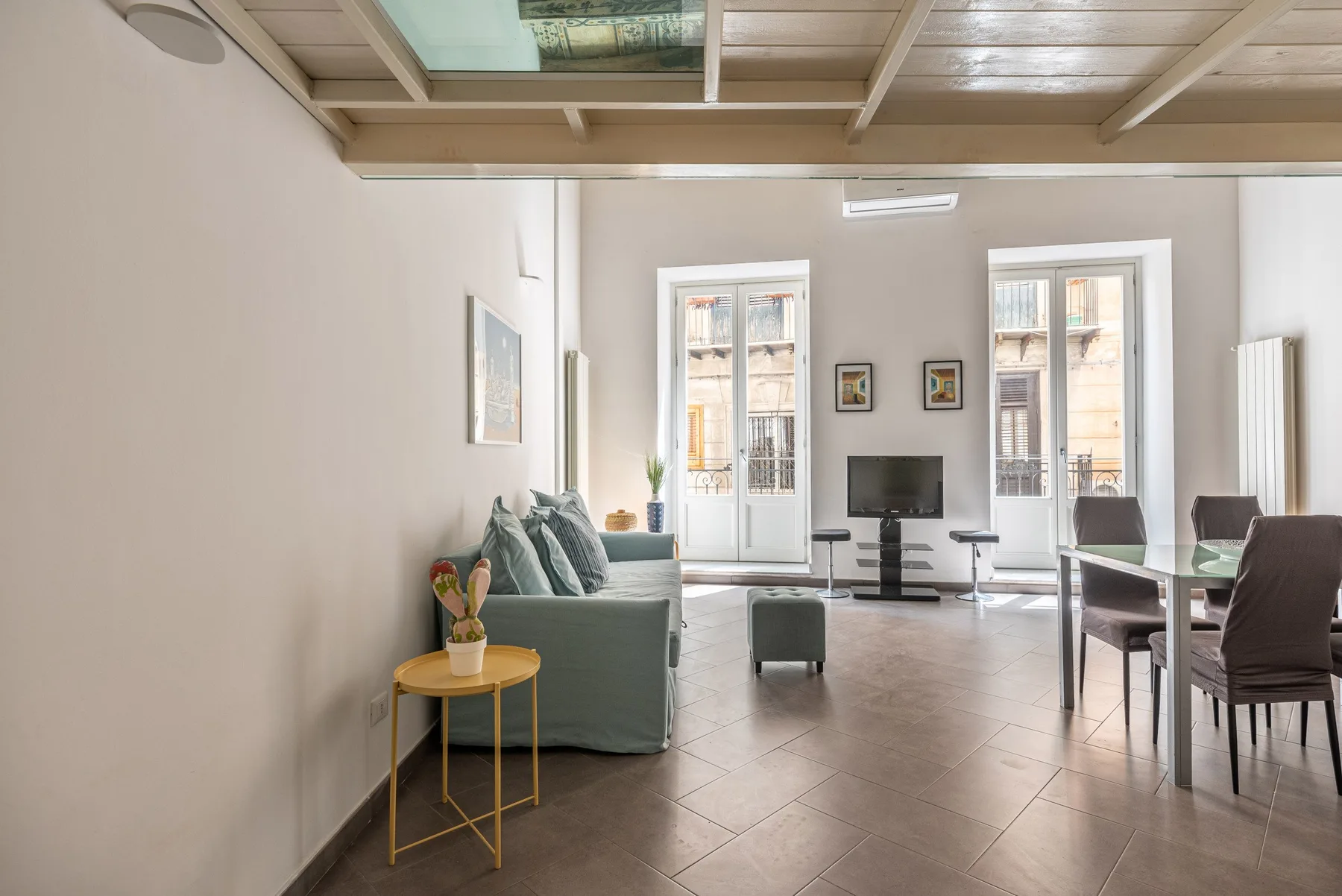 Una luminosa sala de estar y comedor con asientos, un televisor y ventanas altas.