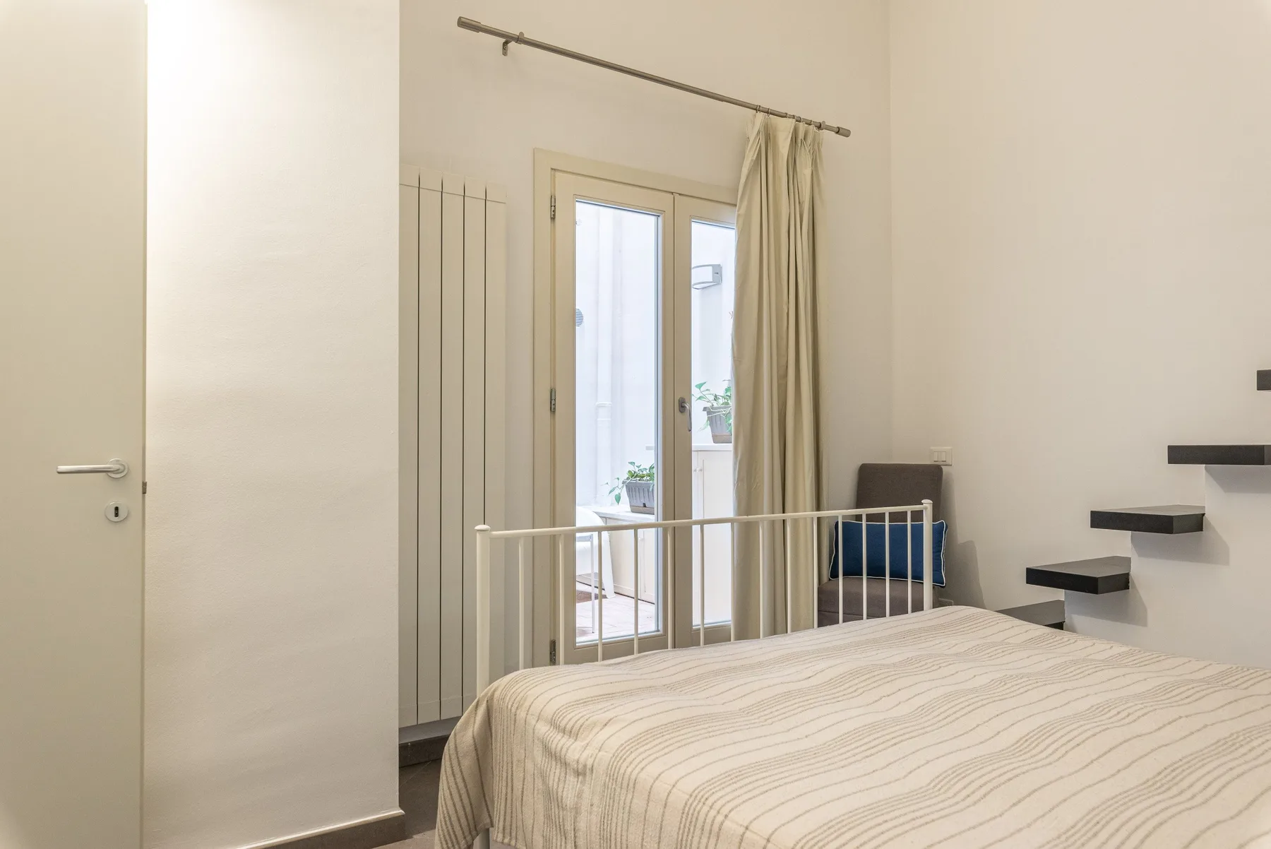 Un dormitorio con una cama junto a una ventana alta y escalones en la pared.