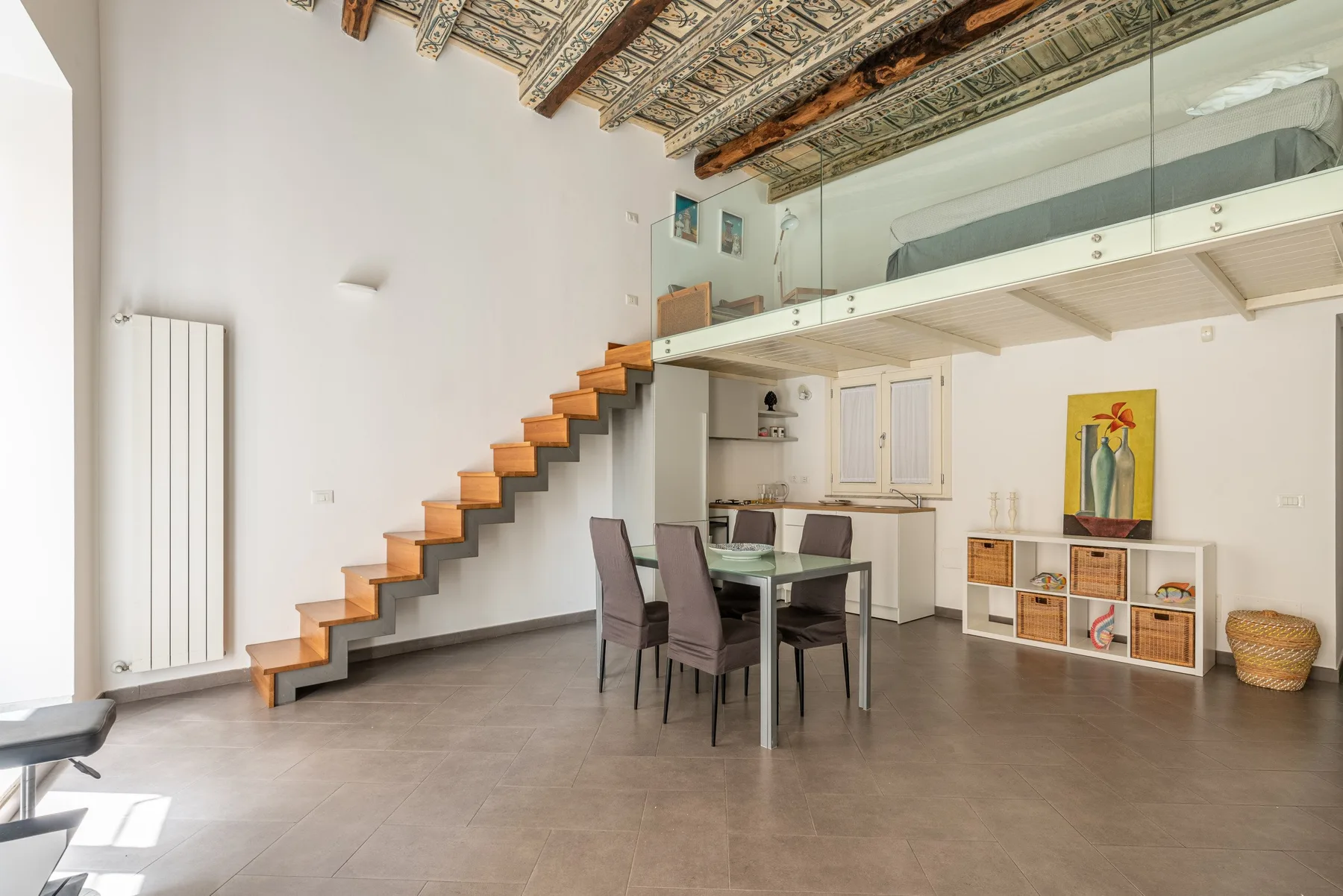 Una habitación diáfana y luminosa tiene una mesa de comedor bajo una escalera de madera y un altillo.