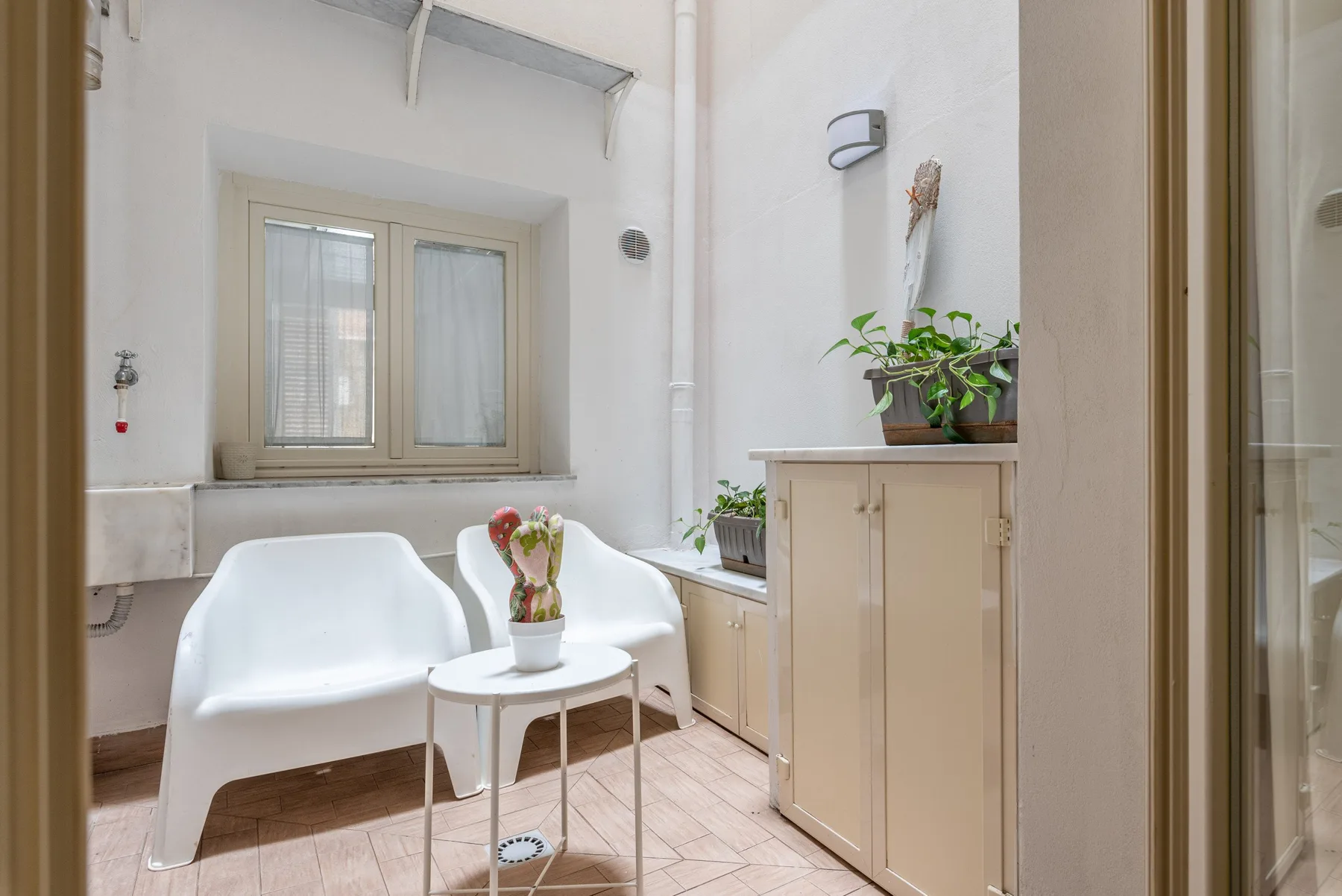 Un baño luminoso con asientos blancos, una mesa pequeña y plantas en macetas.