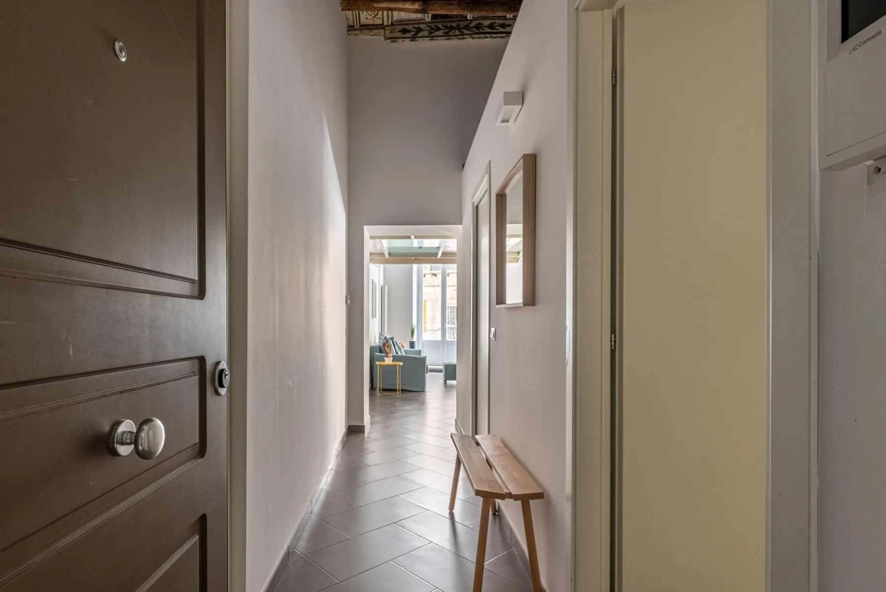 Un pasillo estrecho conduce a una habitación luminosa, con un banco de madera junto a la pared.