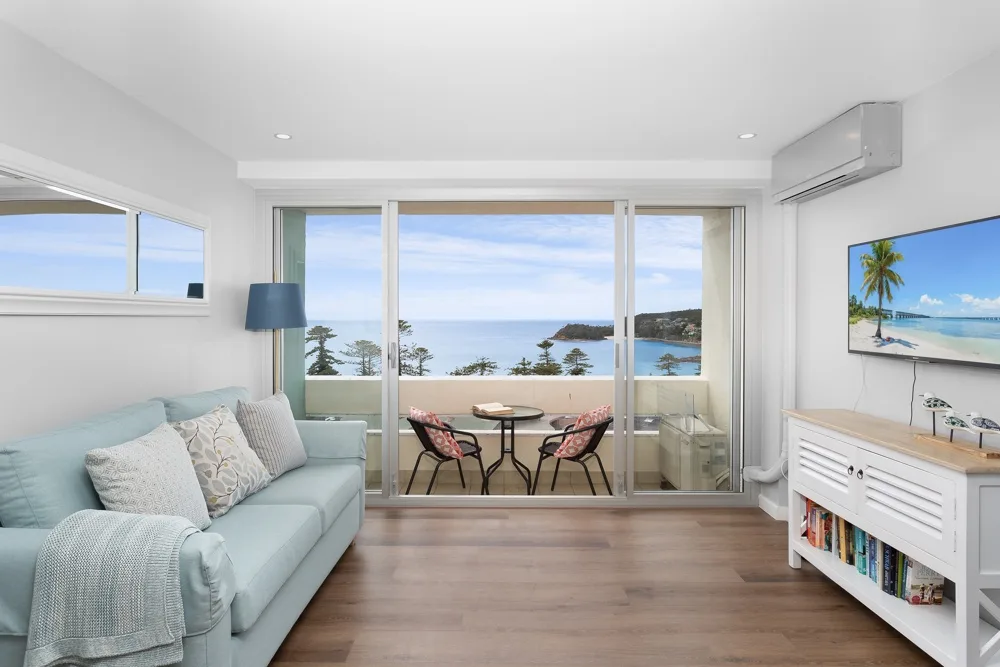 Sala de estar luminosa con asientos junto a grandes ventanales con vistas al mar.