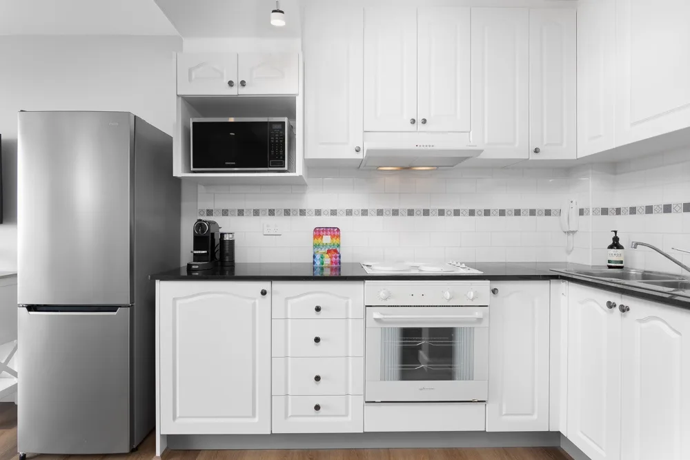 Cocina blanca con gabinetes, horno y refrigerador.