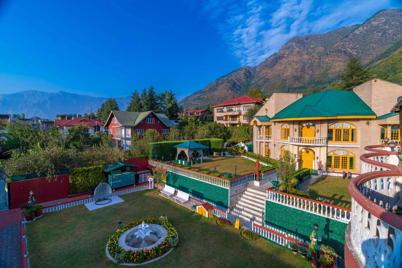 A landscaped courtyard with a circular fountain sits among colorful buildings beneath a mountain.