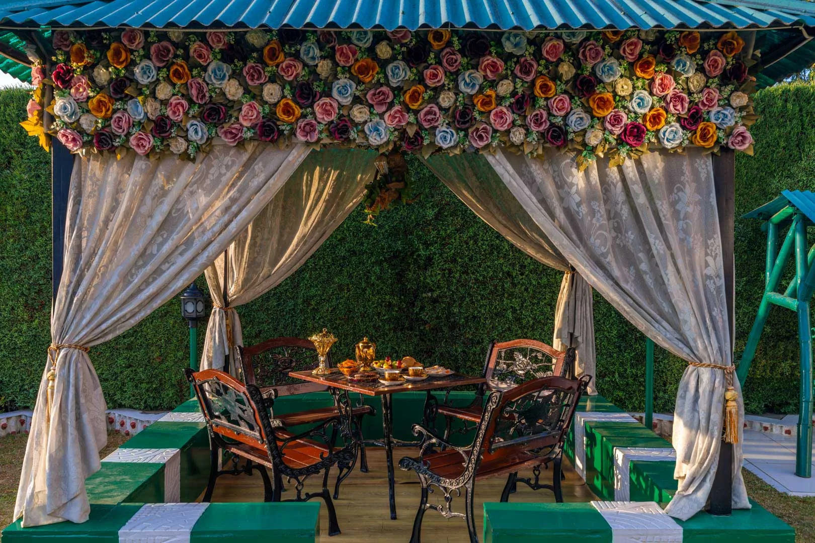 An outdoor dining area sits beneath a flower-trimmed canopy with draped curtains.