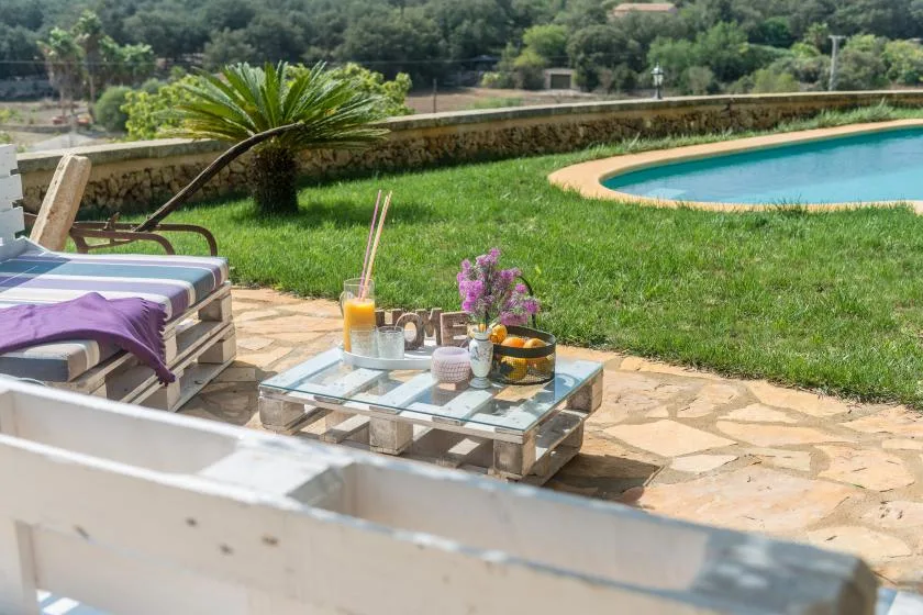 Un patio soleado junto a la piscina tiene asientos y una mesa baja junto al agua.