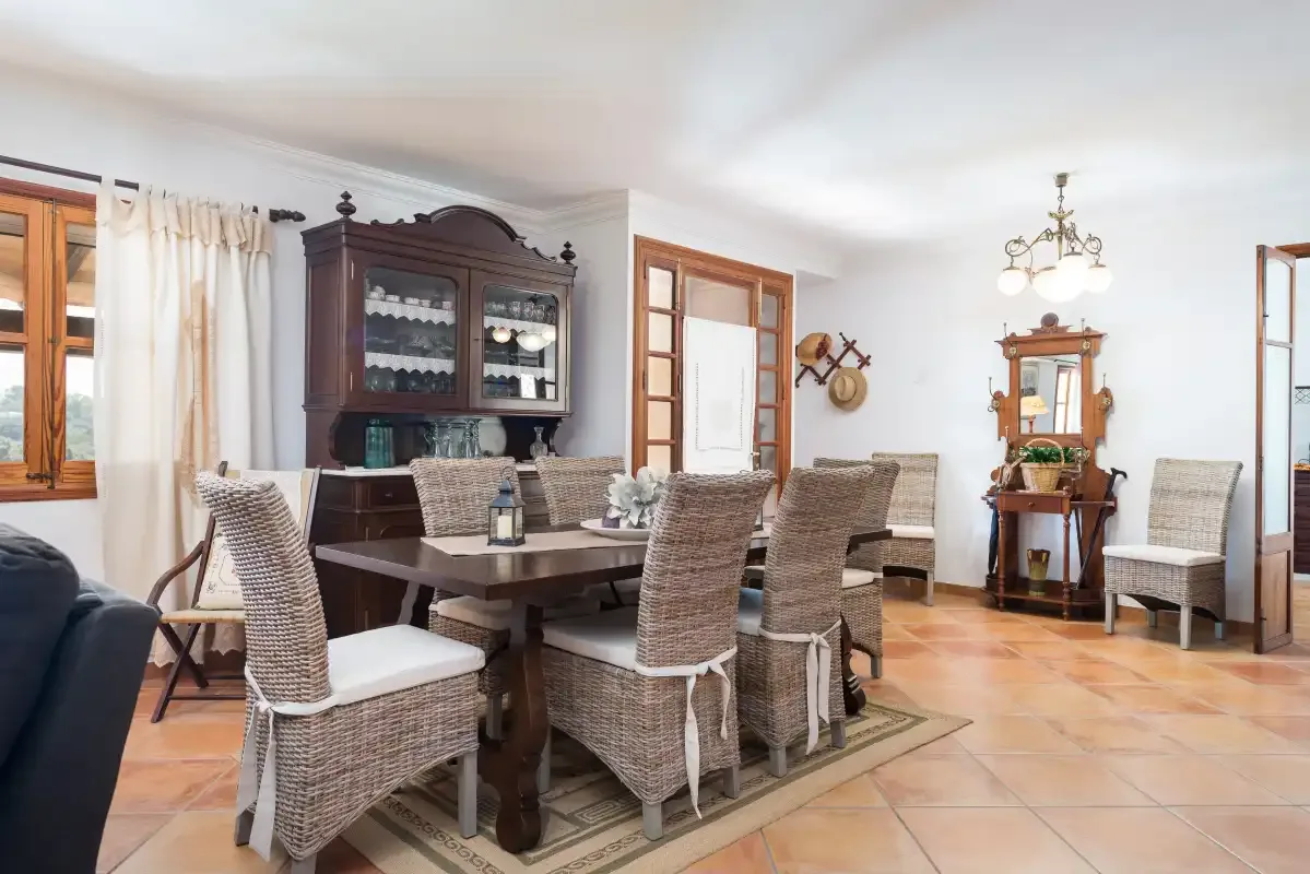 Comedor con una mesa, asientos de mimbre y un aparador oscuro.