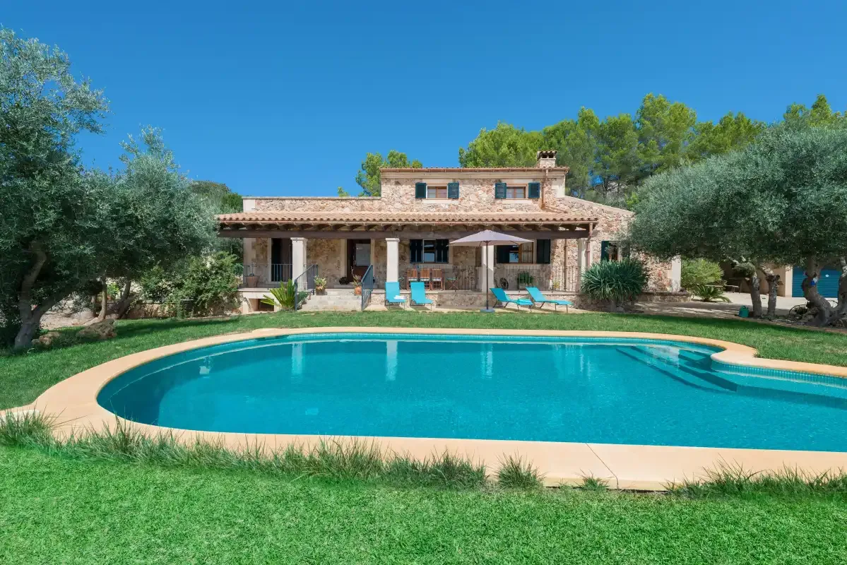 Una casa y una piscina se encuentran en un jardín soleado.