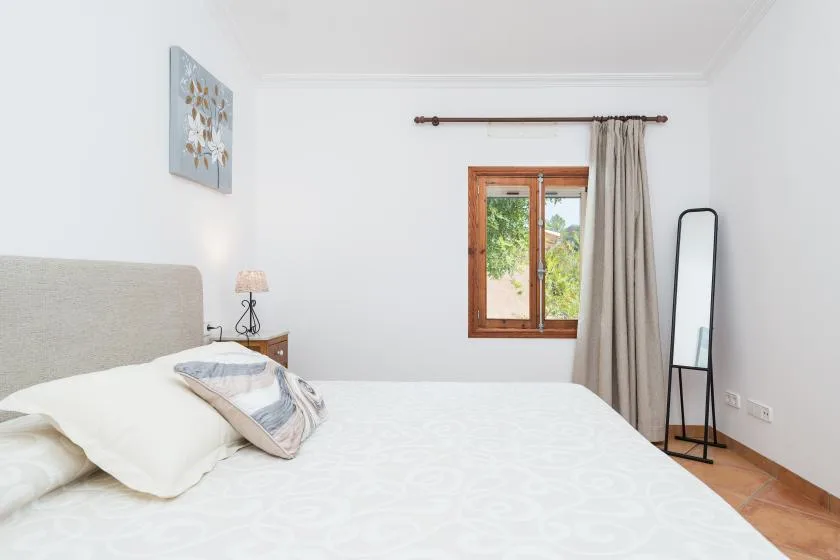 Un dormitorio luminoso con una cama, una ventana de madera y cortinas.