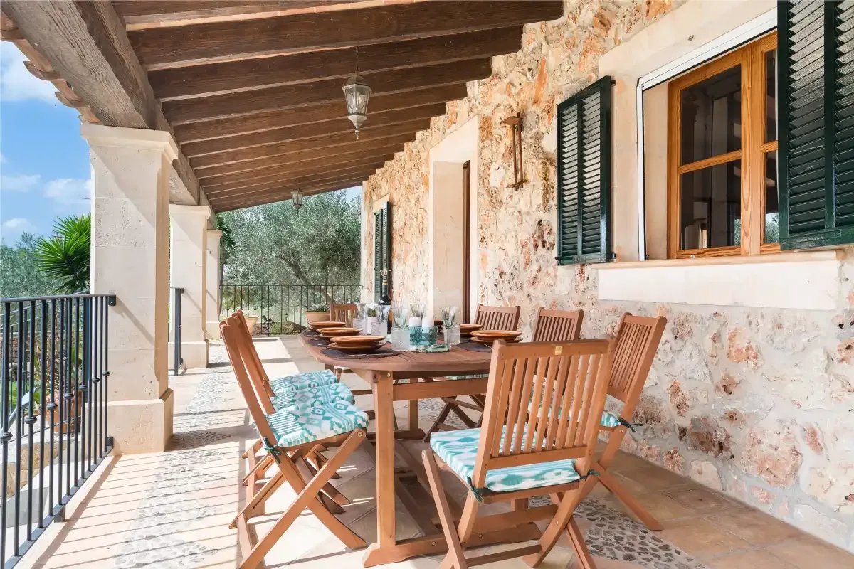 Una zona de comedor exterior cubierta tiene asientos de madera junto a una pared de piedra.