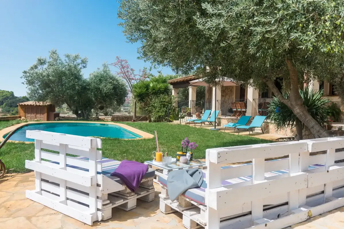 Una zona de piscina ajardinada con asientos junto a una casa sombreada.