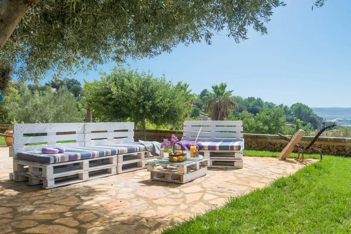 Un patio al aire libre tiene asientos de palés, una mesa baja y vegetación.
