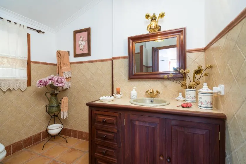Un tocador de baño con lavabo y espejo frente a paredes revestidas de azulejos.