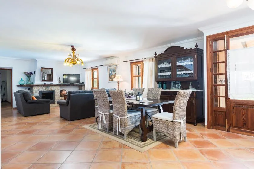 Una zona de comedor y estar cuenta con una mesa, asientos tejidos y un mueble oscuro.