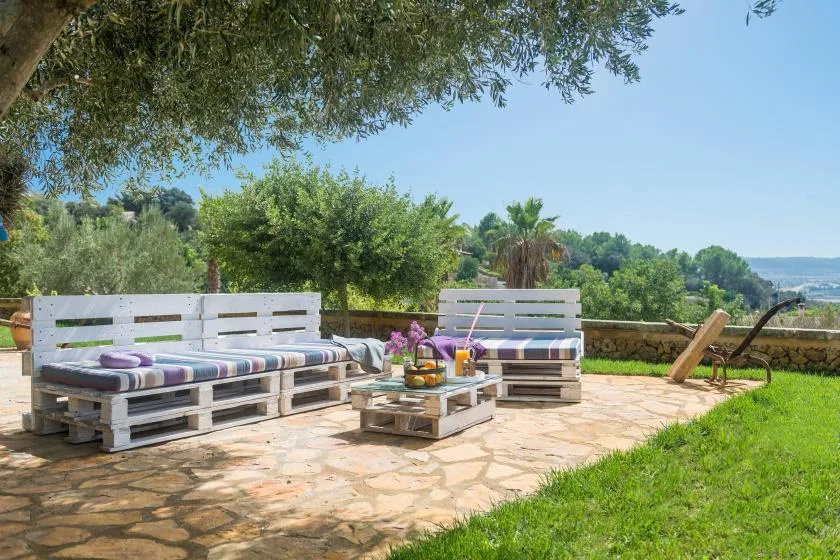 Un patio al aire libre con asientos de palés y una mesa baja da a un paisaje verde.