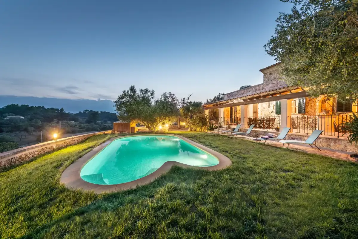 Una casa y una piscina están junto a un jardín con césped al anochecer.