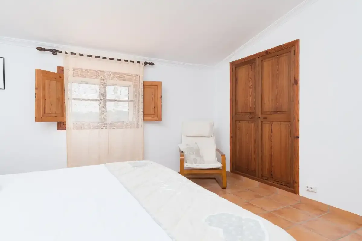 Un dormitorio luminoso con una cama, una ventana y un armario de madera.