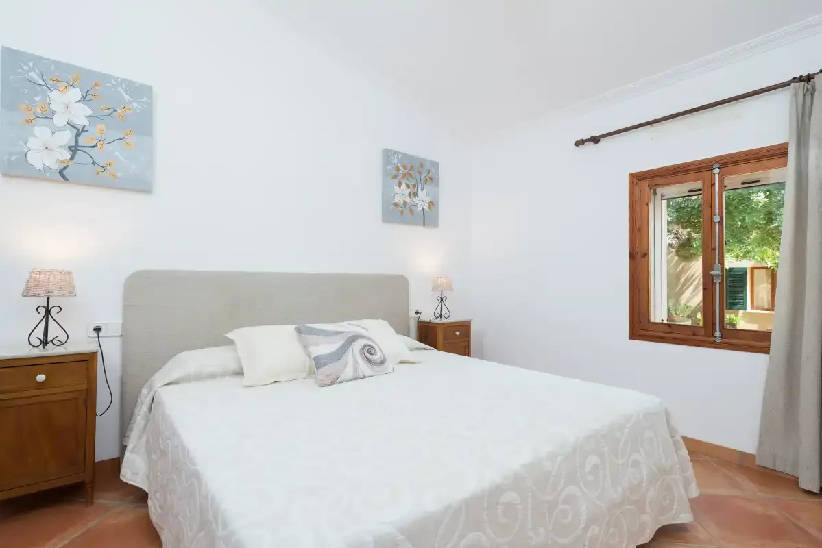 Dormitorio con una cama bien hecha y una ventana con marco de madera.