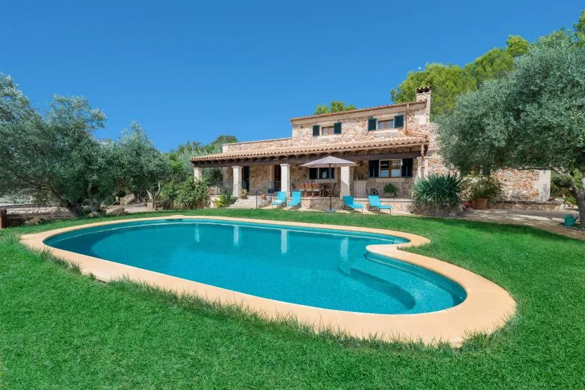 Una piscina está en un jardín con césped frente a una casa de piedra.