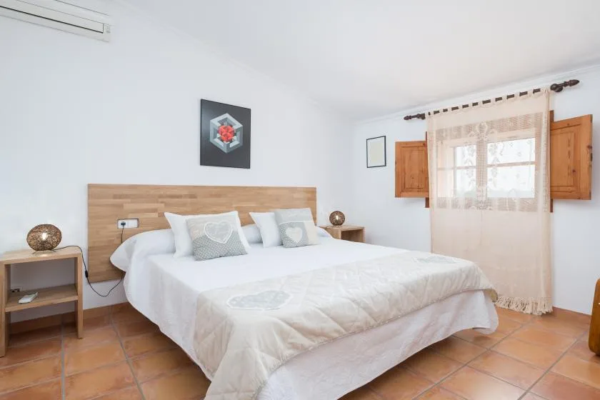 Un dormitorio luminoso con una cama grande, cabecero de madera y una ventana con cortinas.