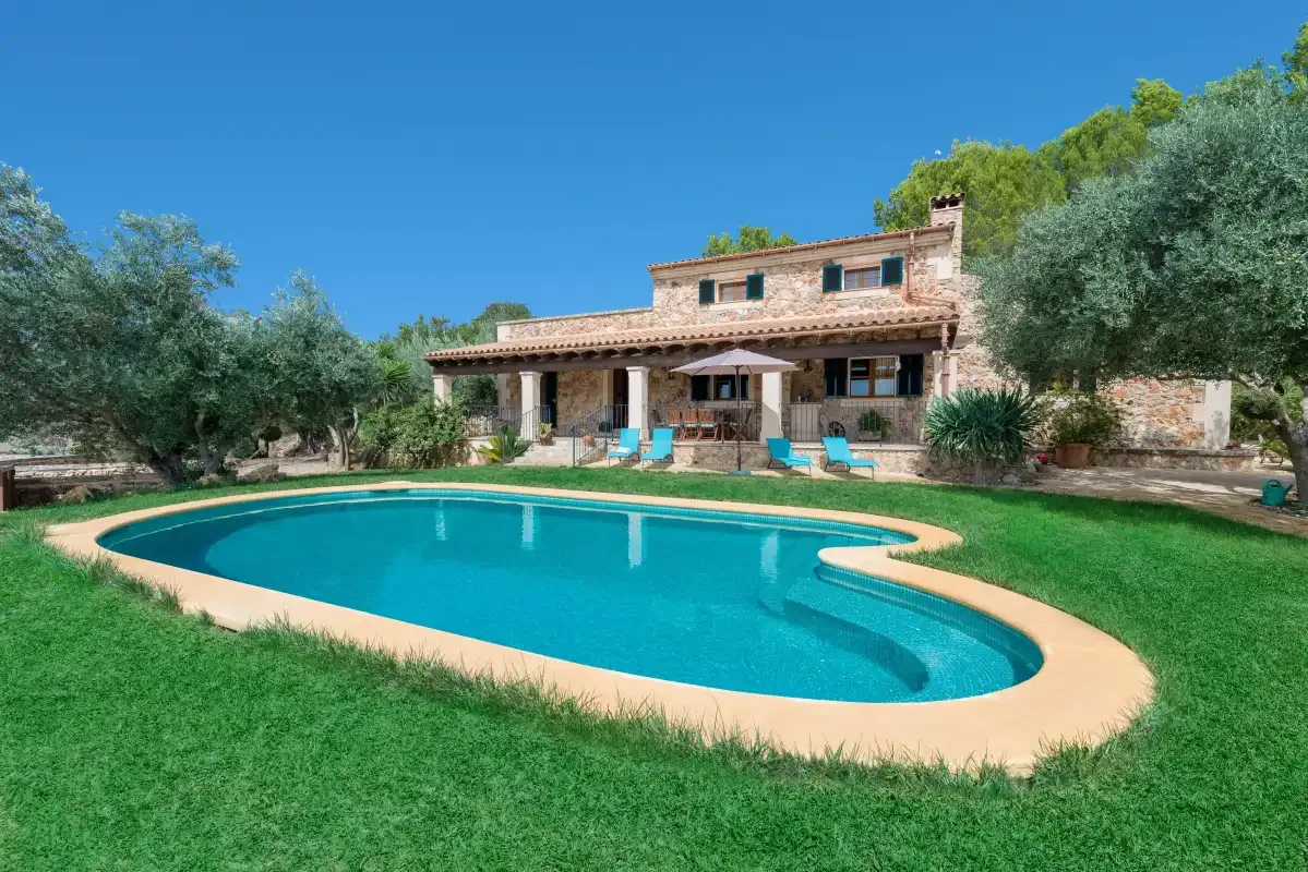 Una piscina está en un césped frente a una casa de piedra.