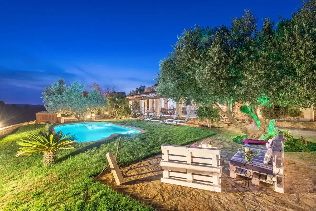 Una piscina y asientos al aire libre están en un jardín junto a una casa.
