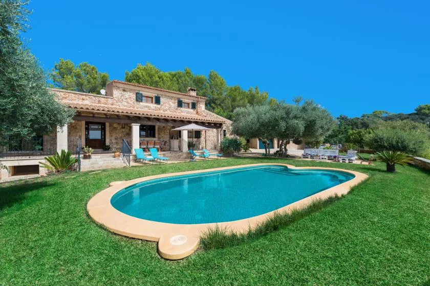 Una piscina está en un césped frente a una casa de piedra.