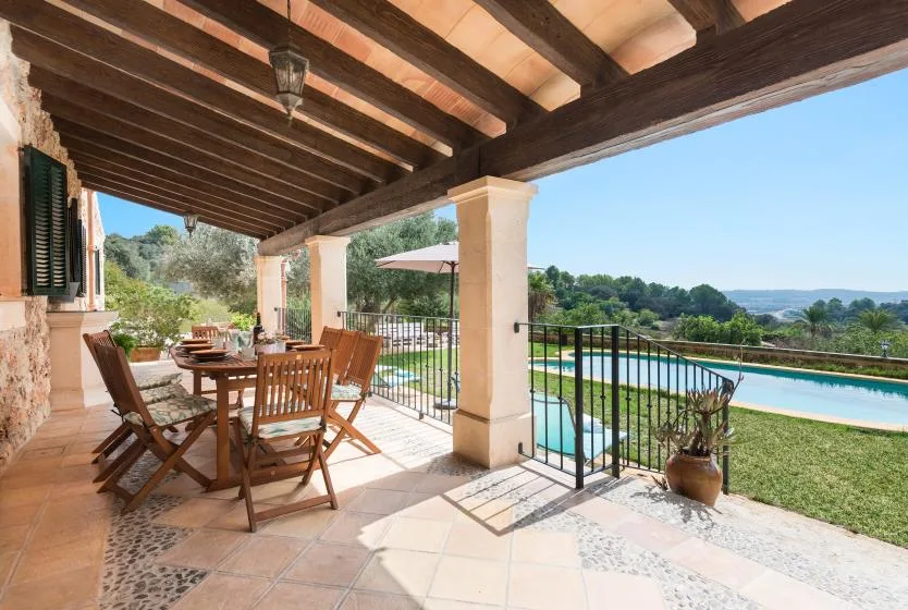 Una zona cubierta de comedor al aire libre da a una piscina y áreas verdes.