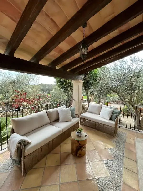 Una zona de estar exterior cubierta da a un jardín y a árboles.