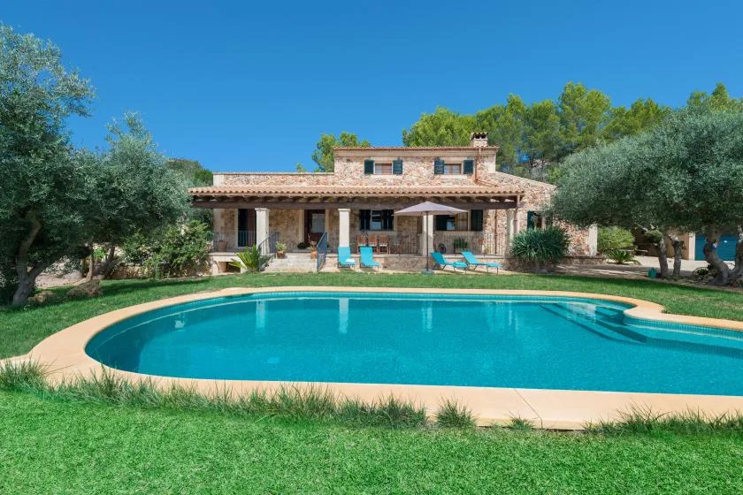 Una casa está detrás de una piscina, con asientos de descanso en el patio.